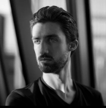 Black-and-white portrait of instructor Stephen Wilcox, bearded with swept-back hair, looking off to the side