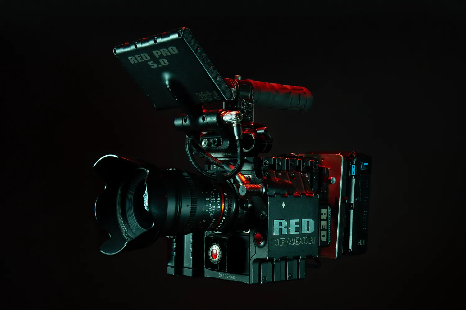 RED Dragon 6K cinema camera with a top handle and RED Pro monitor, lit in red against a black background.