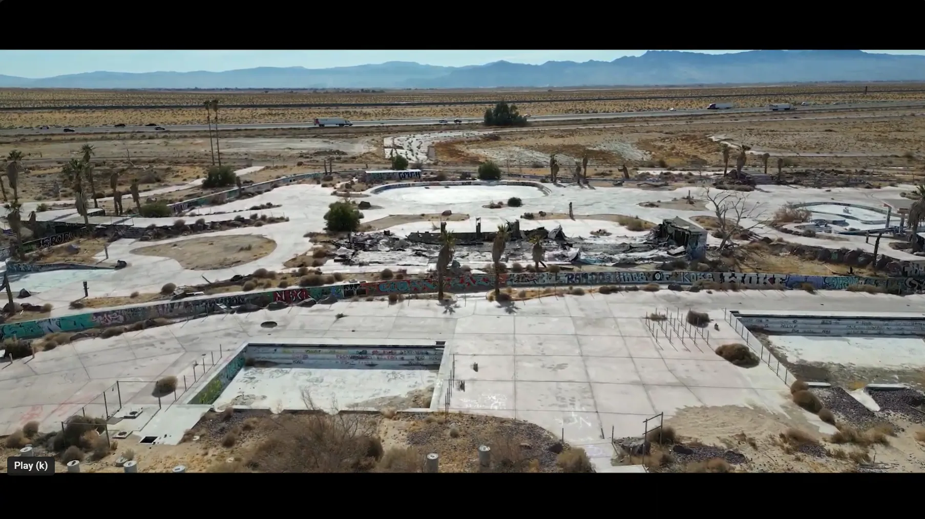 Aerial drone view of the abandoned graffiti-covered water park with empty pools, palm trees and desert mountains behind