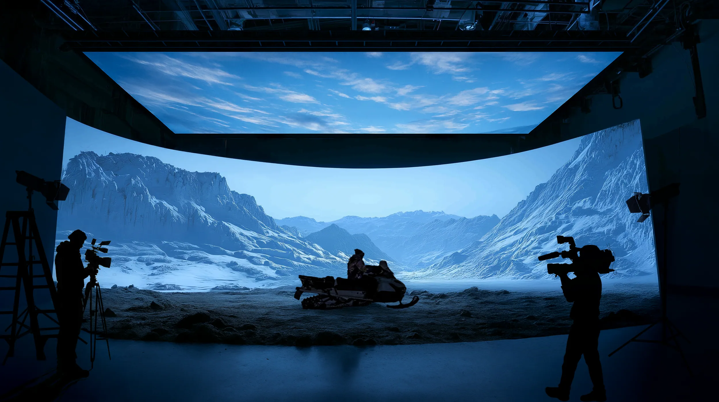 Curved LED wall and ceiling showing snowy mountains behind a snowmobile rider, with two silhouetted camera operators.